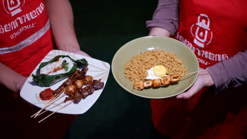 PEDAGANG ANGKRINGAN SEDANG MEMEGANG PIRING BERISI SATE DAN INDOMIE GORENG